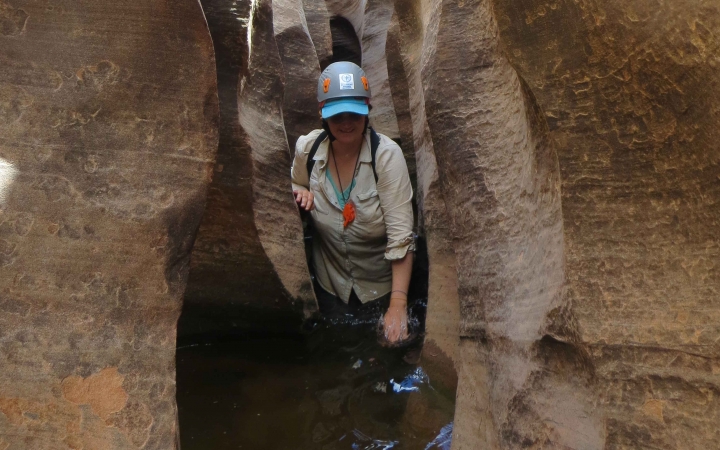 A person makes their way through a narrow canyon in waist-deep water.